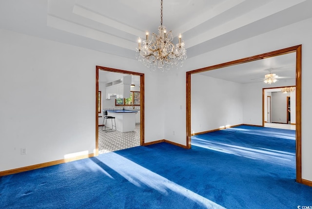 empty room featuring ceiling fan with notable chandelier, a tray ceiling, and carpet floors