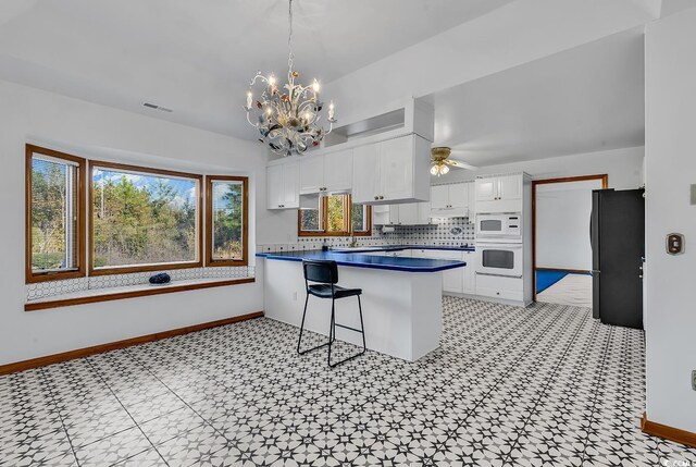 kitchen with white microwave, white cabinets, ceiling fan with notable chandelier, kitchen peninsula, and a breakfast bar area