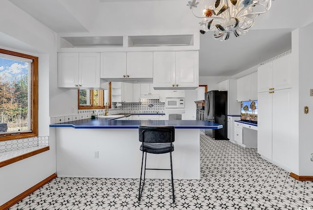 kitchen with white cabinets, a kitchen breakfast bar, white appliances, and kitchen peninsula