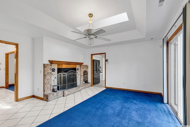 unfurnished living room with a skylight, ceiling fan, a healthy amount of sunlight, light carpet, and a fireplace