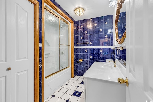 bathroom with tile patterned flooring, vanity, tile walls, and bath / shower combo with glass door