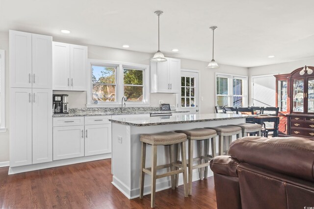 kitchen with pendant lighting, sink, light stone countertops, white cabinets, and a kitchen island