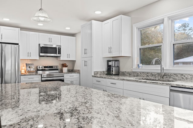 kitchen featuring sink, light stone counters, pendant lighting, stainless steel appliances, and white cabinets