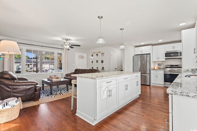 kitchen with hanging light fixtures, appliances with stainless steel finishes, dark hardwood / wood-style floors, light stone countertops, and white cabinets