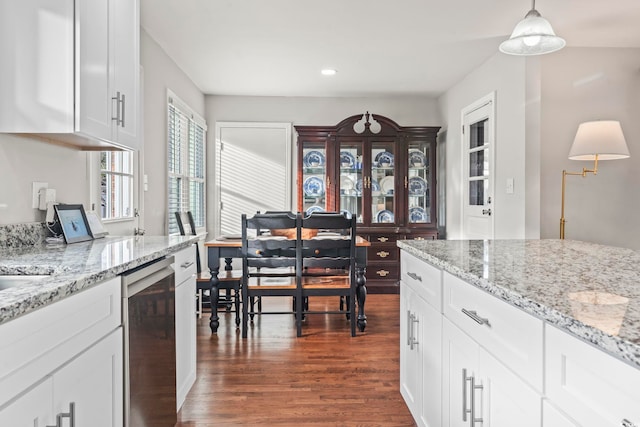 kitchen with dark wood-type flooring, stainless steel dishwasher, pendant lighting, light stone countertops, and white cabinets