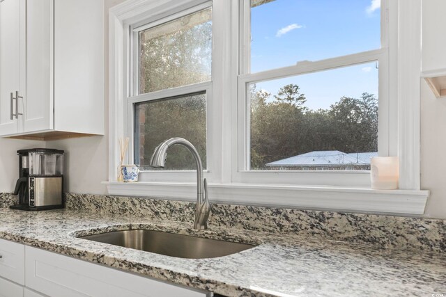 details with white cabinetry, light stone countertops, and sink