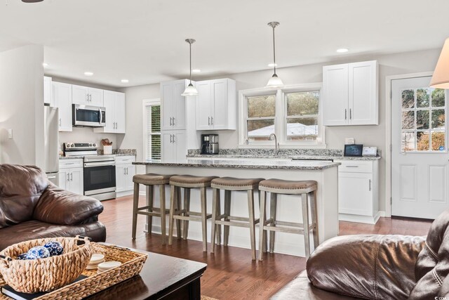 kitchen with white cabinetry, a center island, appliances with stainless steel finishes, pendant lighting, and light stone countertops