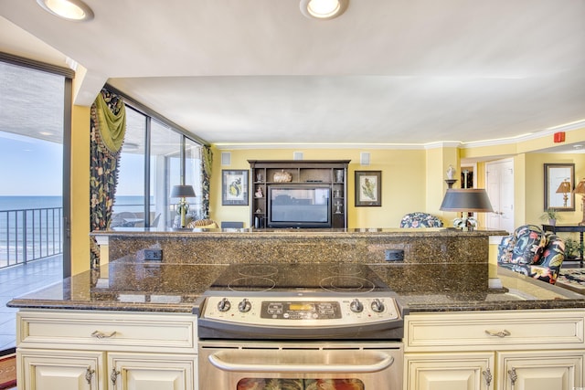 kitchen featuring stainless steel electric stove, a water view, dark stone countertops, ornamental molding, and cream cabinetry