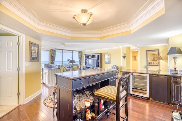 kitchen with wine cooler, stainless steel fridge, wood-type flooring, a kitchen island, and ornamental molding