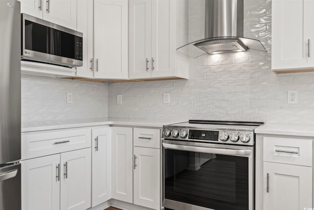 kitchen with white cabinets, appliances with stainless steel finishes, backsplash, and wall chimney range hood