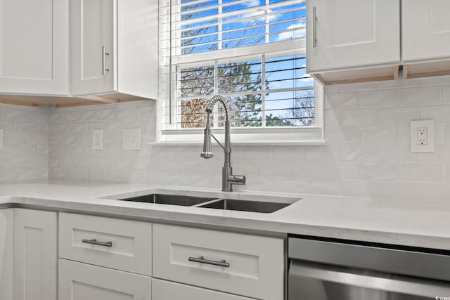 kitchen featuring light stone countertops, white cabinetry, stainless steel dishwasher, and sink