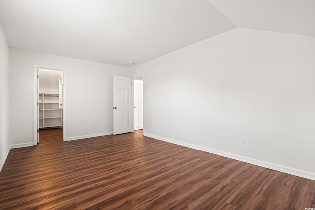 unfurnished bedroom featuring lofted ceiling, a walk in closet, a closet, and dark wood-type flooring