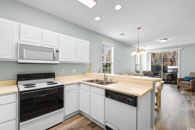 kitchen featuring white appliances, sink, white cabinetry, light hardwood / wood-style floors, and kitchen peninsula