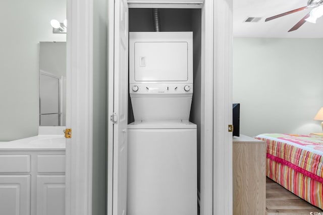 laundry room with light wood-type flooring, ceiling fan, stacked washer and clothes dryer, and sink