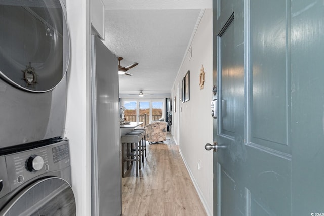 laundry area featuring a textured ceiling, ceiling fan, light hardwood / wood-style floors, and stacked washer / dryer