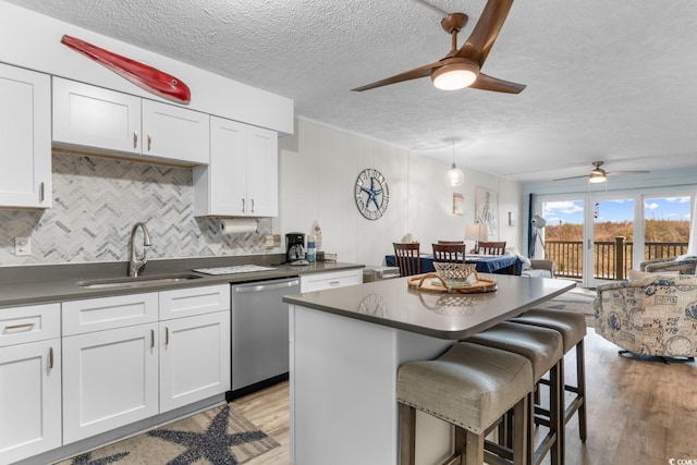 kitchen featuring dishwasher, sink, light wood-type flooring, white cabinetry, and a breakfast bar area