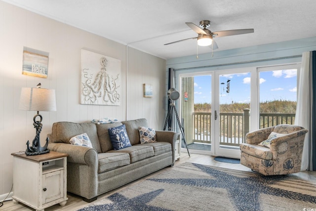 living room with a textured ceiling, light wood-type flooring, and ceiling fan