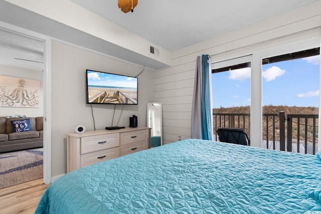 bedroom with access to outside, wooden walls, ceiling fan, and light wood-type flooring