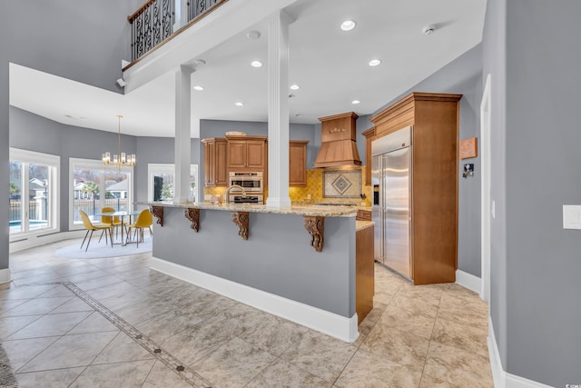 kitchen with a kitchen bar, appliances with stainless steel finishes, tasteful backsplash, light stone counters, and custom range hood