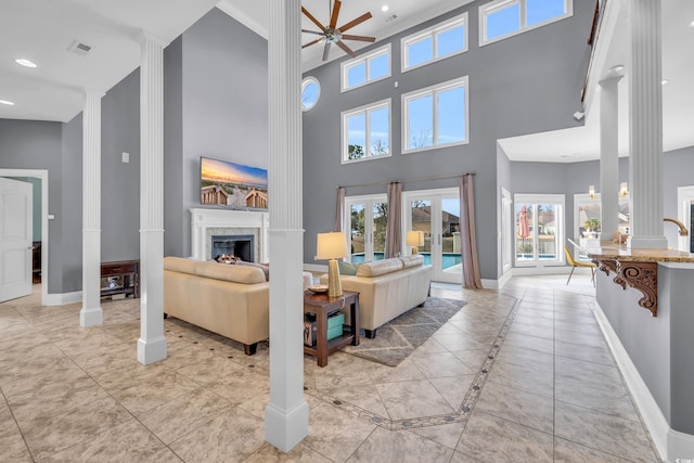 tiled living room featuring ceiling fan, ornate columns, and a high ceiling