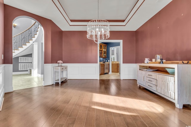 unfurnished dining area featuring wood-type flooring, an inviting chandelier, and a raised ceiling