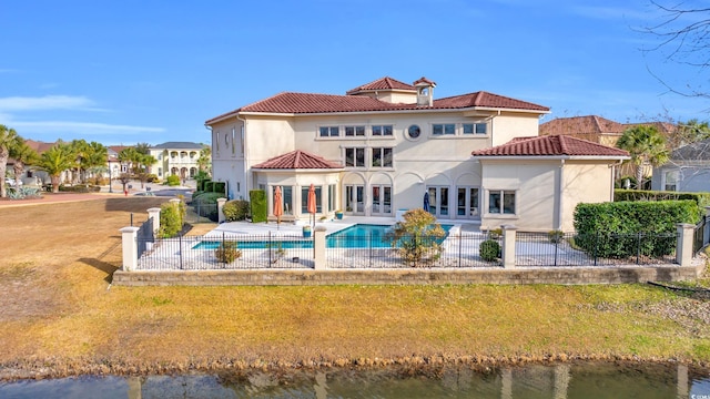 rear view of house featuring a lawn, french doors, a fenced in pool, a water view, and a patio