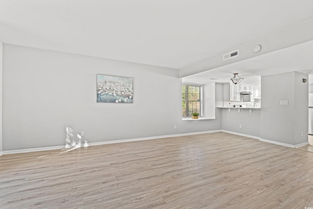 unfurnished living room with a chandelier and light hardwood / wood-style flooring