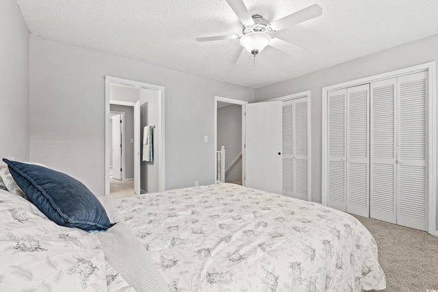 bedroom with ceiling fan, light carpet, two closets, and a textured ceiling