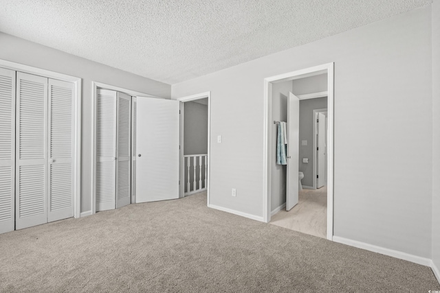 unfurnished bedroom featuring multiple closets, light colored carpet, and a textured ceiling