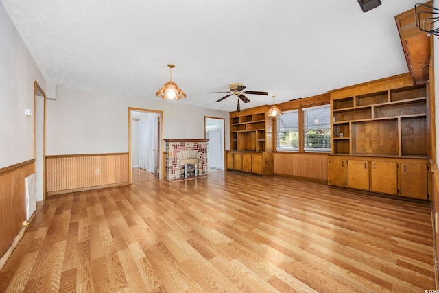 unfurnished living room with wooden walls, ceiling fan, light wood-type flooring, built in features, and a fireplace