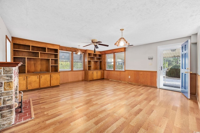 unfurnished living room featuring built in shelves, a textured ceiling, light hardwood / wood-style flooring, and a stone fireplace