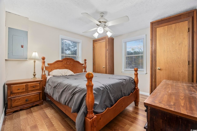 bedroom with electric panel, ceiling fan, light hardwood / wood-style flooring, and a textured ceiling