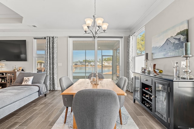 dining room featuring crown molding, dark wood-type flooring, a water view, a chandelier, and bar area