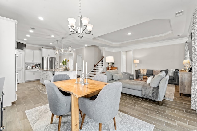 dining room with a notable chandelier, light hardwood / wood-style flooring, crown molding, and a tray ceiling