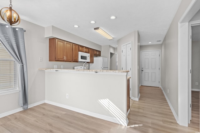 kitchen featuring light hardwood / wood-style floors, light stone counters, white appliances, and kitchen peninsula