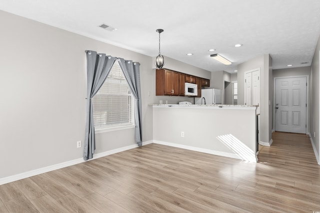 kitchen with kitchen peninsula, light stone counters, white appliances, light hardwood / wood-style floors, and hanging light fixtures