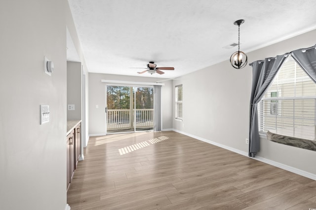 unfurnished living room featuring ceiling fan with notable chandelier and light hardwood / wood-style flooring