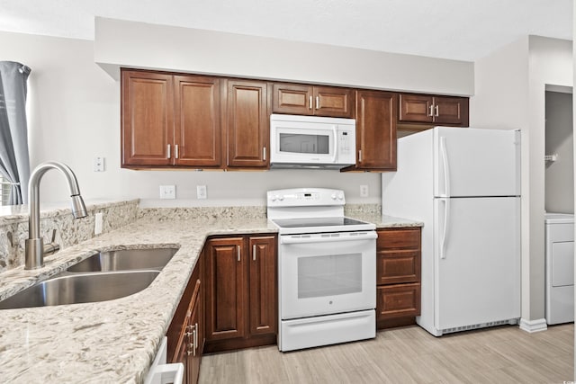 kitchen with white appliances, sink, light wood-type flooring, light stone counters, and washer / clothes dryer