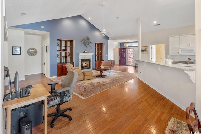 home office with a high end fireplace, light hardwood / wood-style flooring, ceiling fan, and lofted ceiling