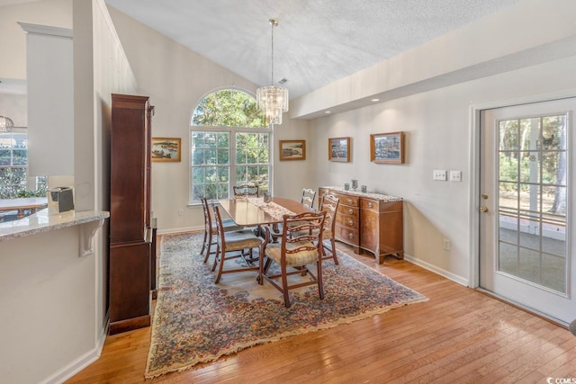 dining room featuring a textured ceiling, light wood-type flooring, an inviting chandelier, and vaulted ceiling