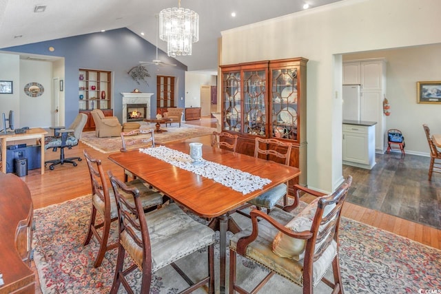 dining room featuring hardwood / wood-style flooring, ceiling fan with notable chandelier, and high vaulted ceiling