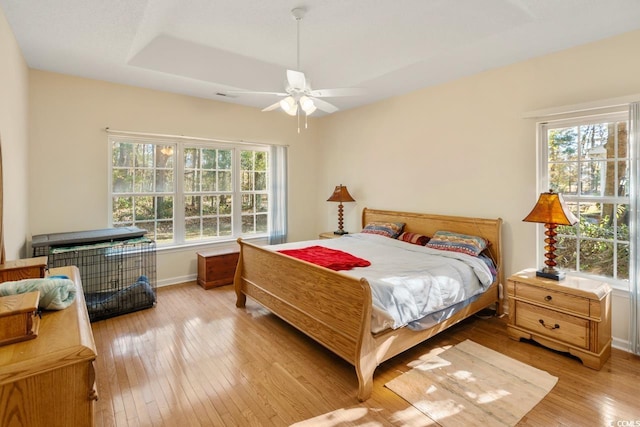 bedroom with a tray ceiling, multiple windows, ceiling fan, and light hardwood / wood-style floors