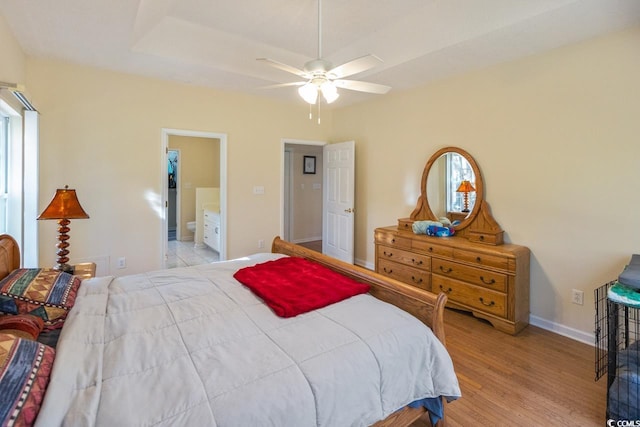 bedroom featuring ensuite bathroom, a raised ceiling, ceiling fan, and light hardwood / wood-style floors