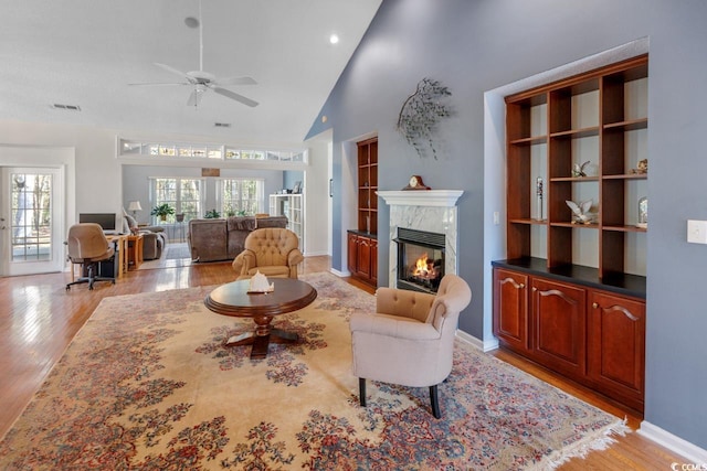 living room with ceiling fan, light hardwood / wood-style floors, a premium fireplace, and a wealth of natural light