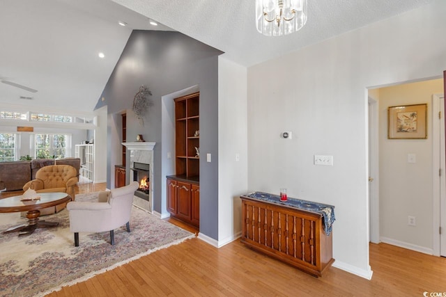 living room featuring a premium fireplace, lofted ceiling, a textured ceiling, ceiling fan with notable chandelier, and light wood-type flooring