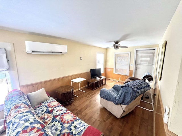 living room featuring a wall mounted air conditioner, ceiling fan, wood walls, and wood-type flooring