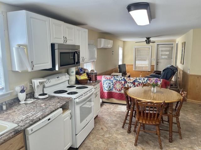 kitchen with wood walls, plenty of natural light, white cabinets, and white appliances