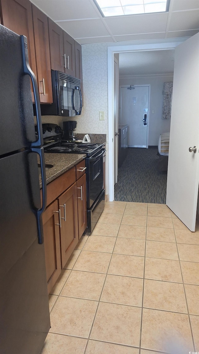 kitchen with light tile patterned floors, a drop ceiling, dark stone countertops, and black appliances