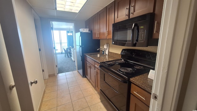 kitchen featuring black appliances, dark stone countertops, light tile patterned floors, and sink