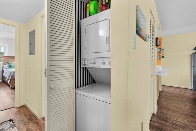 laundry room with electric panel, stacked washer and dryer, and dark hardwood / wood-style floors